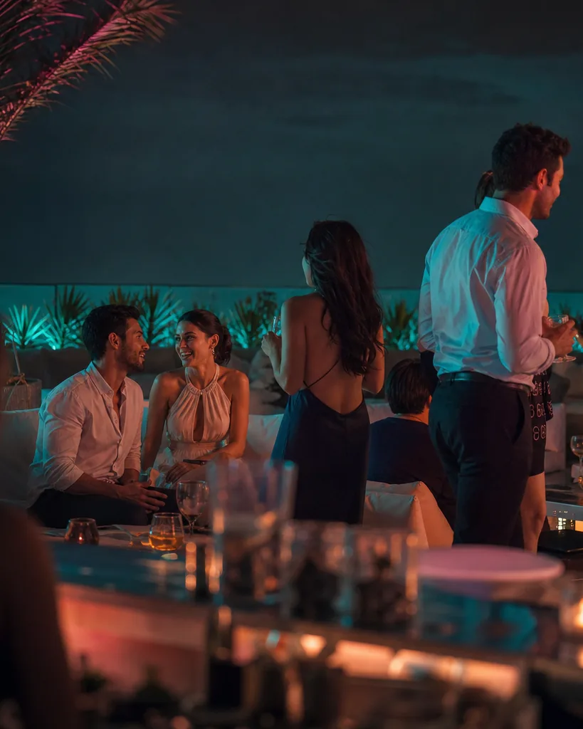 Adults in summer evening clothes on a Miami style rooftop at night with pink and teal light